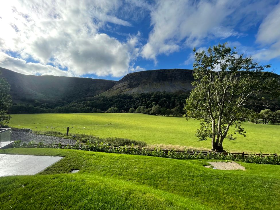 A grassy garden with a tree and a gravel path overlooking a field with sheep and hills in the background at Pennant Uchaf in Pennant near Llanbrynmair