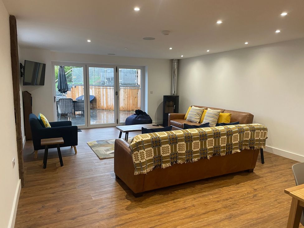 A living room with brown leather sofas, a black armchair, a television on the wall, a coffee table, and sliding glass doors leading to an outdoor patio at Pennant Uchaf in Pennant near Llanbrynmair