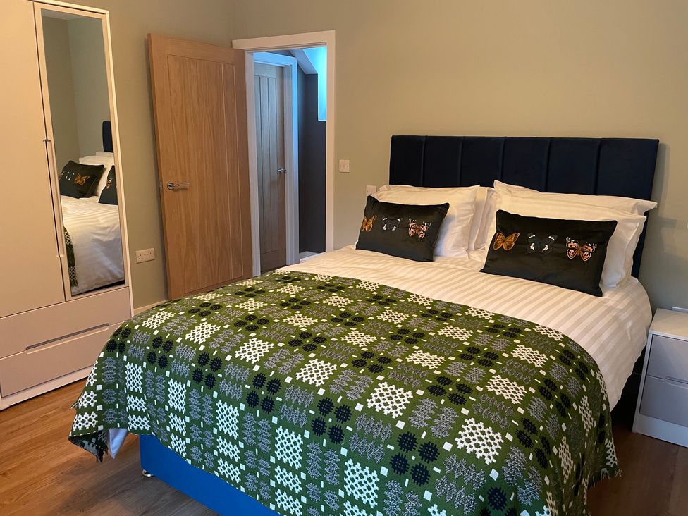 A bedroom with a bed with butterfly cushions and a green patterned blanket a wardrobe with mirror and wooden doors at Pennant Uchaf in Pennant near Llanbrynmair