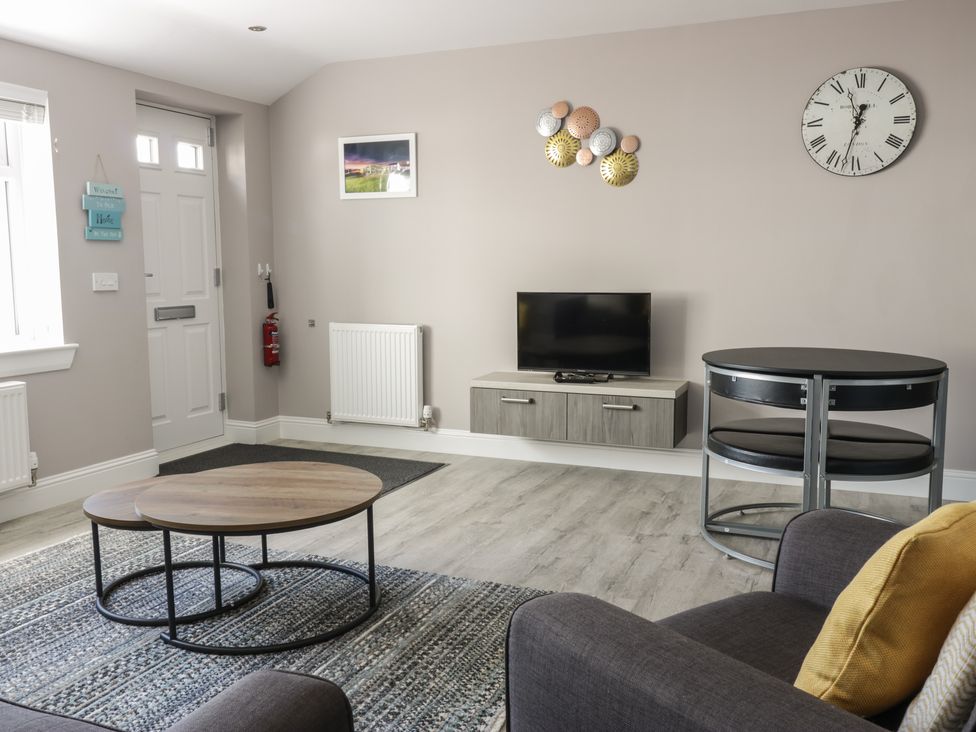 A living room with nested coffee tables rug and a wall-mounted tv at Seascape in Kinghorn
