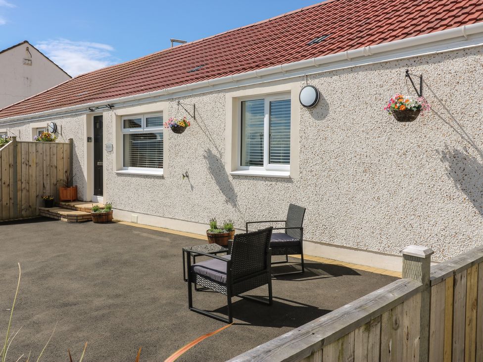 A patio area with two chairs and a small table outside a building with hanging flower baskets at Seascape in Kinghorn