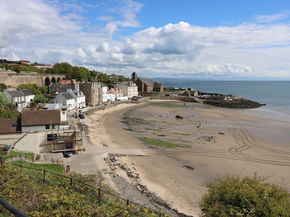 A beach with tire tracks and a promenade near houses and a church by the sea at Seascape in Kinghorn