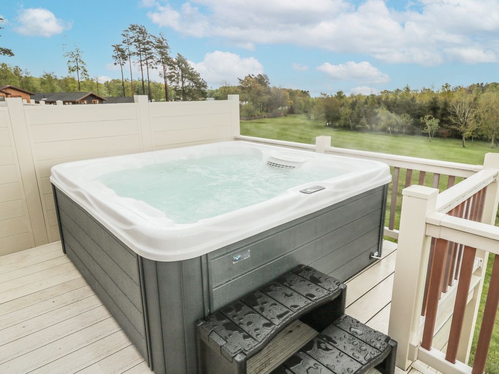 An outdoor hot tub on a wooden deck with plastic stairs and a view of a grassy field and trees at Woodland View Lodge Swarland near Felton