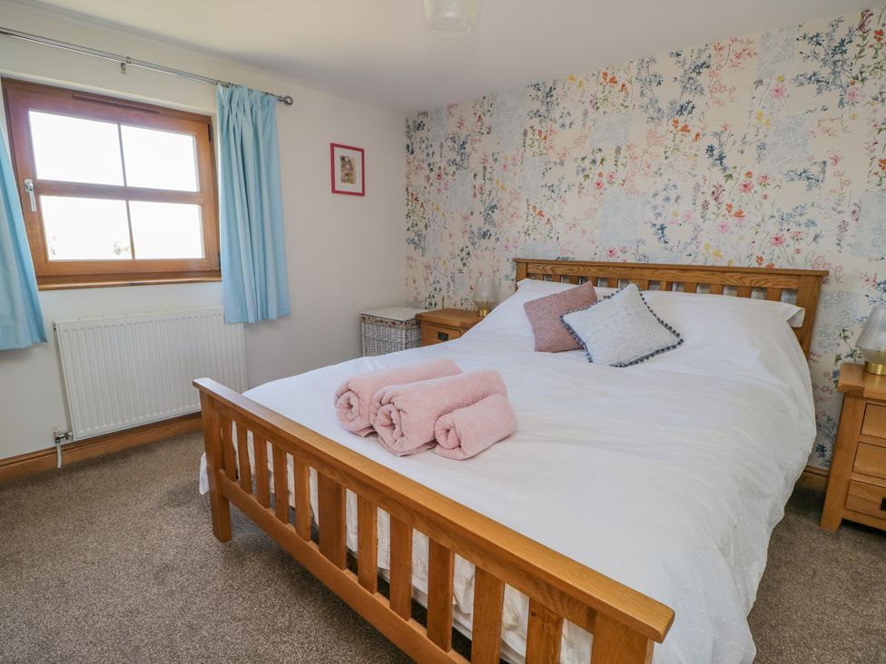 A bedroom with a wooden bed frame white bedding pink rolled towels blue curtains and floral wallpaper at Bramblewood Cottage in Crookdake near Bassenthwaite