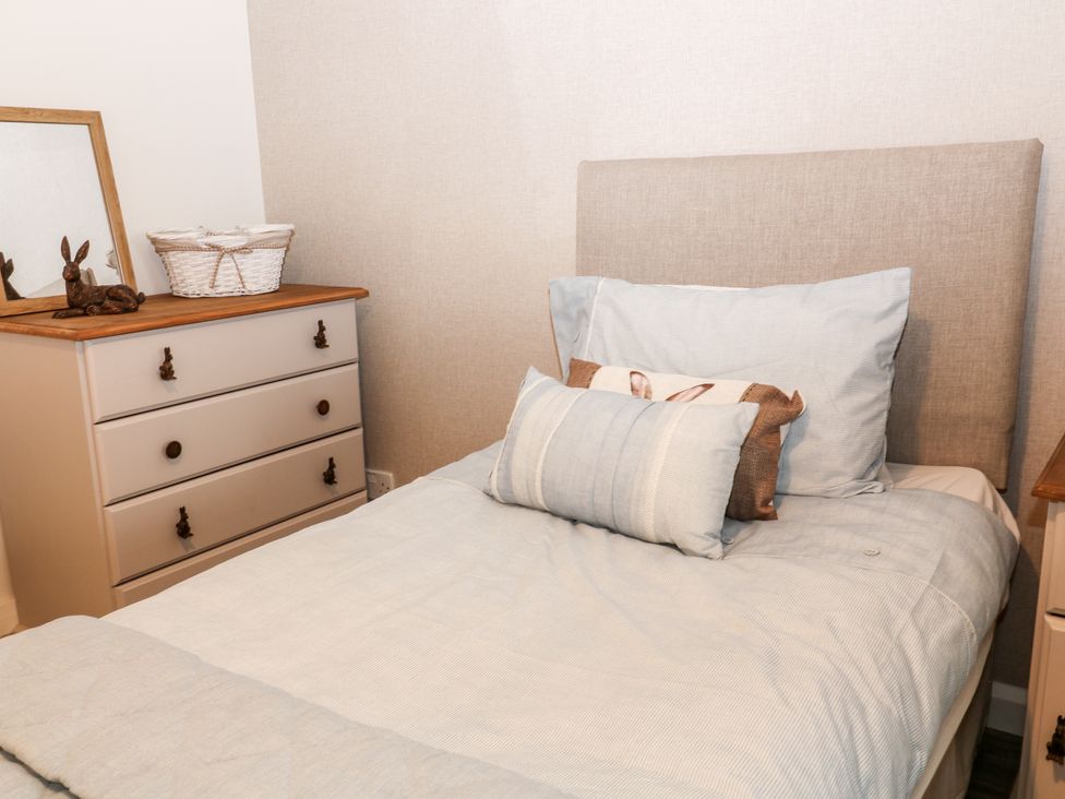 A bedroom with a bed and a chest of drawers with a mirror and basket on top at Lavender Lodge in St Ann's Chapel Cornwall