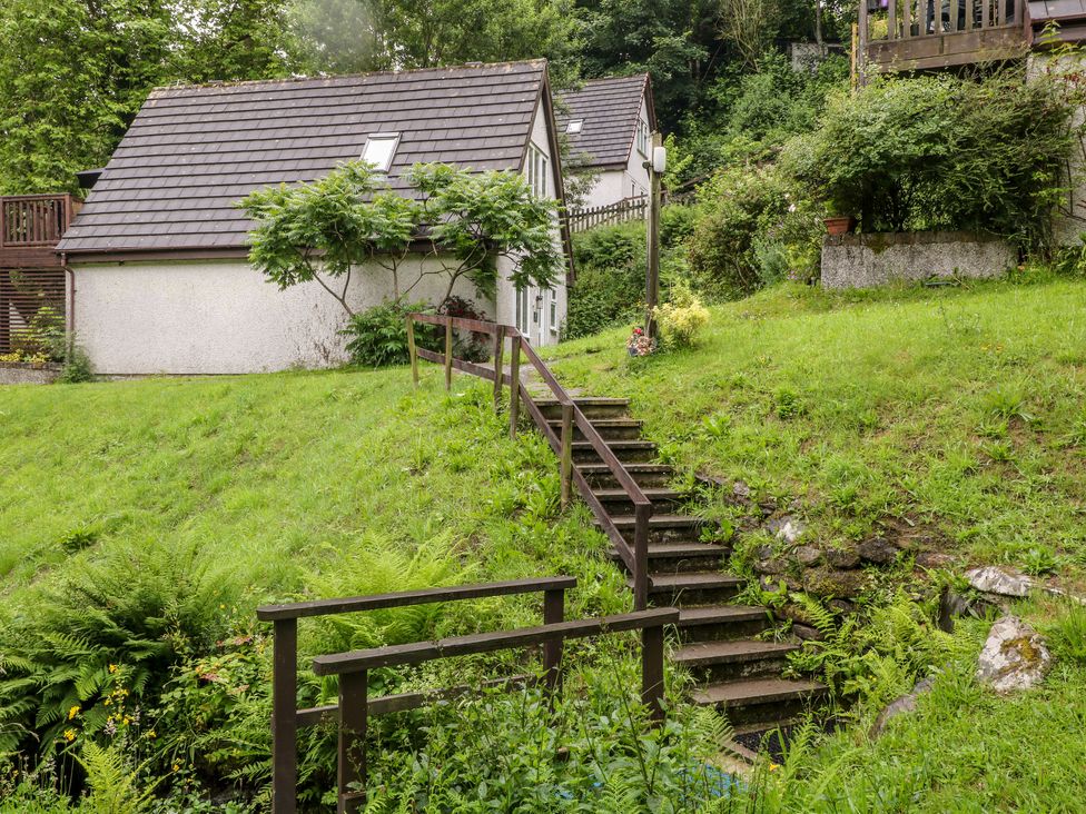 A wooden staircase with handrails leading up a grassy slope to a house surrounded by trees and plants at Lavender Lodge in St Ann's Chapel Cornwall