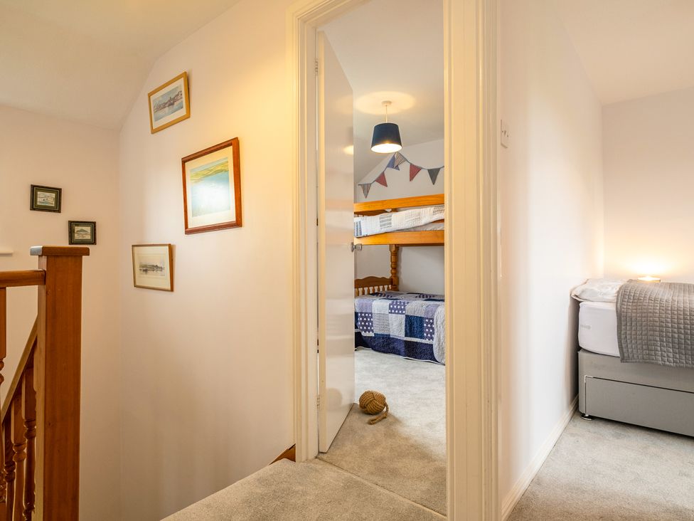 A hallway with framed pictures on the wall leading to a bedroom with bunk beds and another room with a bed at Hazelhurst Rock