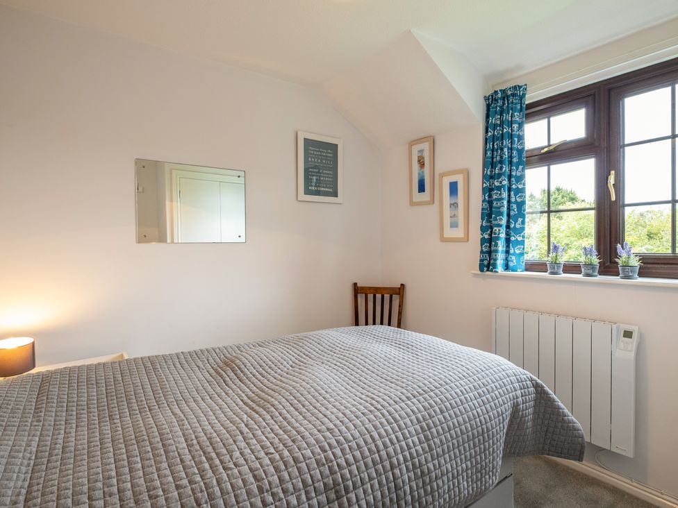 A bedroom with a bed covered in a gray quilt next to a window with blue curtains and three small plants on the windowsill at Hazelhurst in Rock