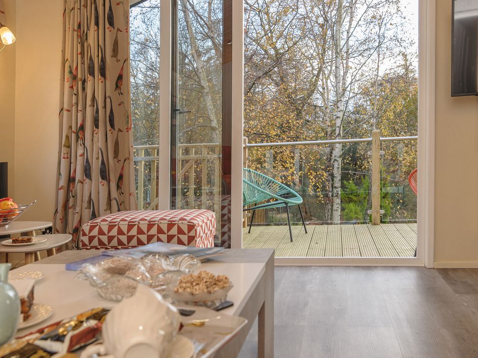 A living room with a red and white patterned ottoman and glass doors opening to a balcony with chairs and trees outside at Oaks One Swarland near Felton