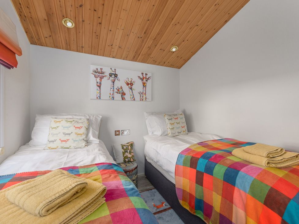 A bedroom with two single beds colorful blankets and giraffe artwork on the wall at Oaks One Swarland near Felton