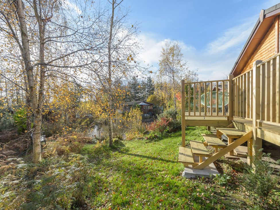 A wooden deck with chair and stairs leading to a garden with trees and grassy area at Oaks One Swarland near Felton