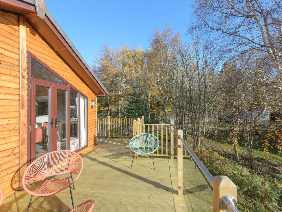 A wooden deck with three chairs outside a cabin surrounded by trees at Oaks One Swarland near Felton