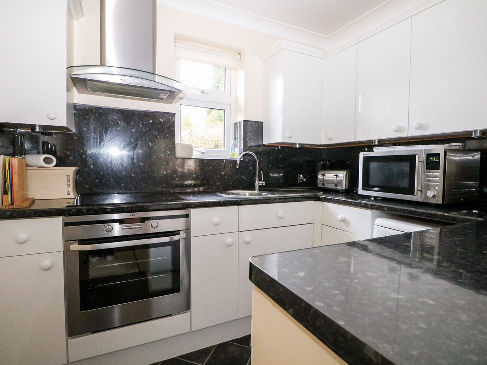 A kitchen with white cabinets black countertops a stainless steel oven microwave and toaster at Heath Retreat in Buxted
