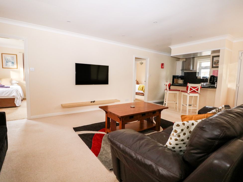 A living room with a wall mounted TV wooden coffee table leather sofa and an open kitchen area at Heath Retreat in Buxted