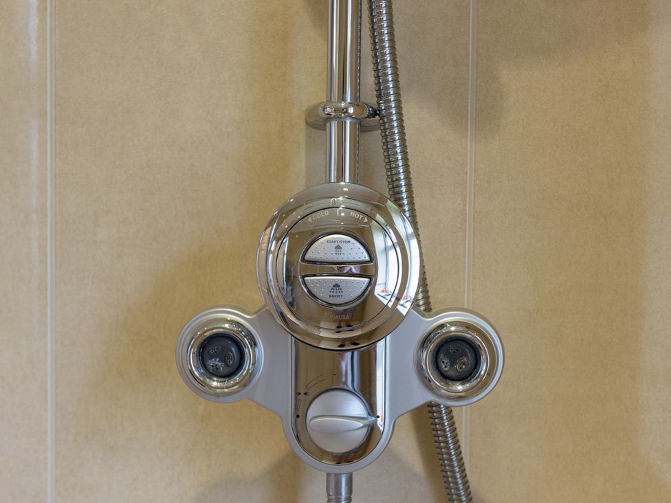A close up of a chrome shower control panel mounted on a beige tiled wall at Heath Retreat in Buxted