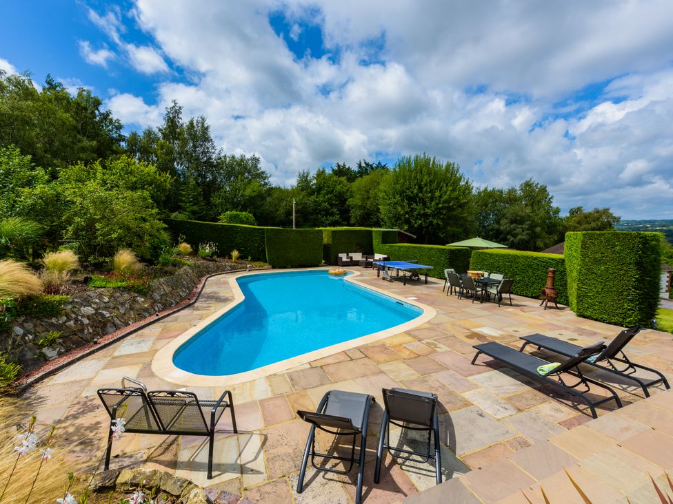 An outdoor swimming pool with lounge chairs table tennis and dining table surrounded by hedge at Heath Retreat in Buxted