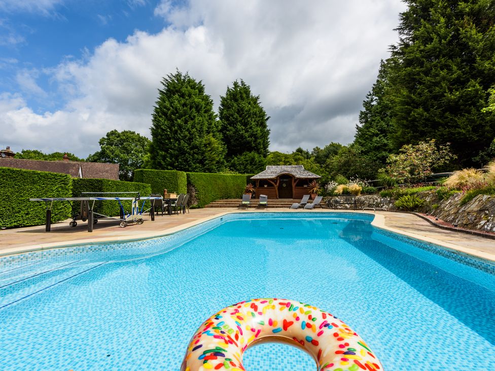 An outdoor swimming pool with a donut float a table tennis table and seating area in a garden at Heath Retreat in Buxted