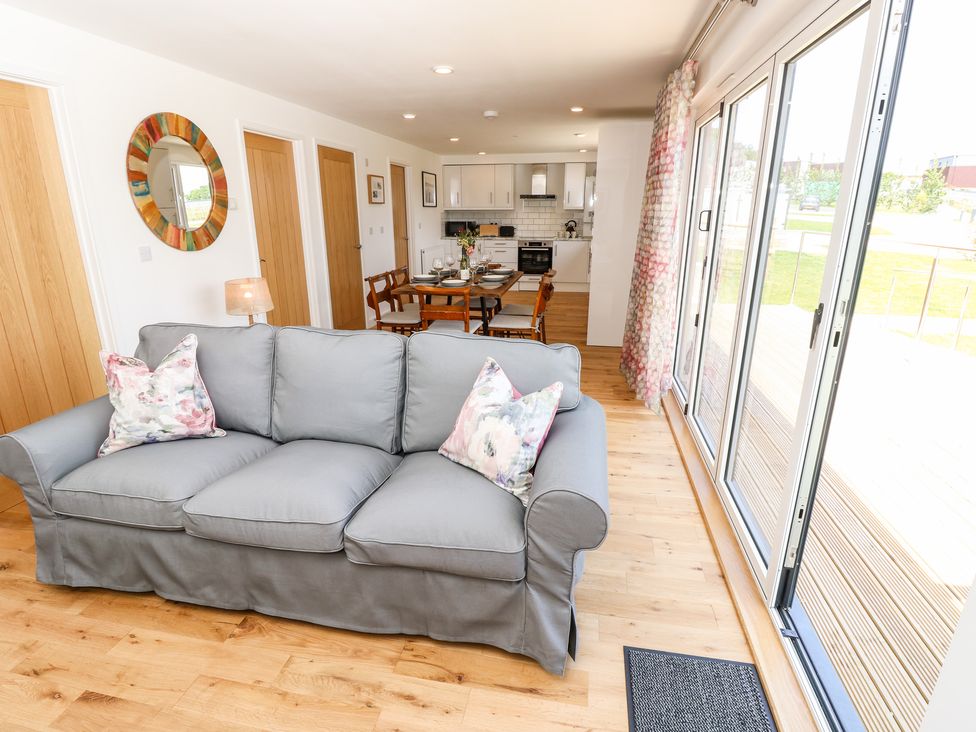 A living area with a gray sofa and floral pillows next to a dining table and kitchen with wooden doors and large sliding glass doors at Chianti in Seaview
