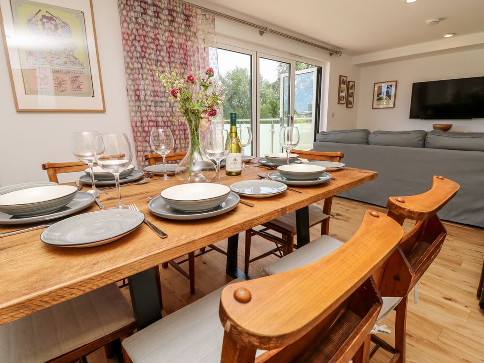 A dining table set with plates glasses and a wine bottle in a room with a gray sofa and a wall mounted TV at Chianti in Seaview
