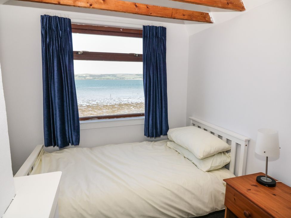 A bedroom with a bed pillows a nightstand with a lamp and a window showing a sea view at Waters Edge in Stranraer