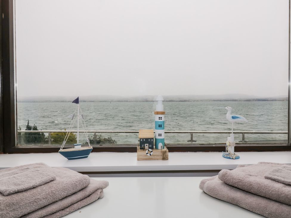 A window view of the sea with small nautical decorations and folded towels on a white surface at Waters Edge in Stranraer