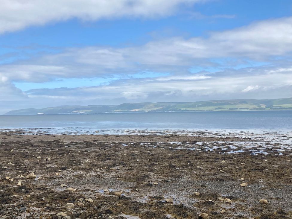 A rocky shore with seaweed and water leading to distant hills under a cloudy sky at Waters Edge in Stranraer