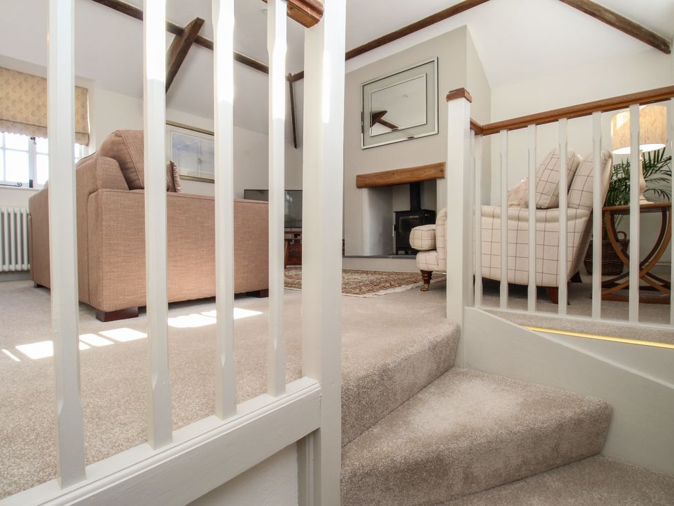 A living room with beige sofas a fireplace and a small staircase at The Coach House at Lackington Farm in Piddletrenthide