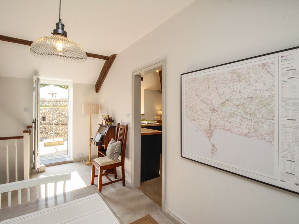 A room with a wooden chair and a small desk near an open door showing an outdoor umbrella and swing at The Coach House at Lackington Farm Piddletrenthide