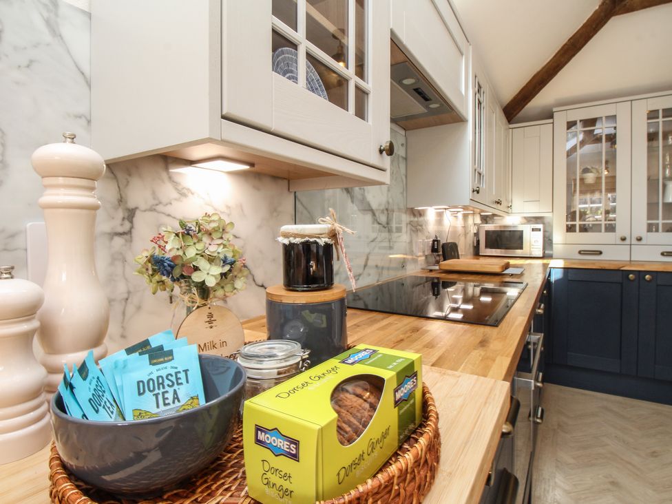 A kitchen countertop with tea packets in a bowl ginger biscuits and jars with cabinets and a microwave in the background at The Coach House at Lackington Farm in Piddletrenthide