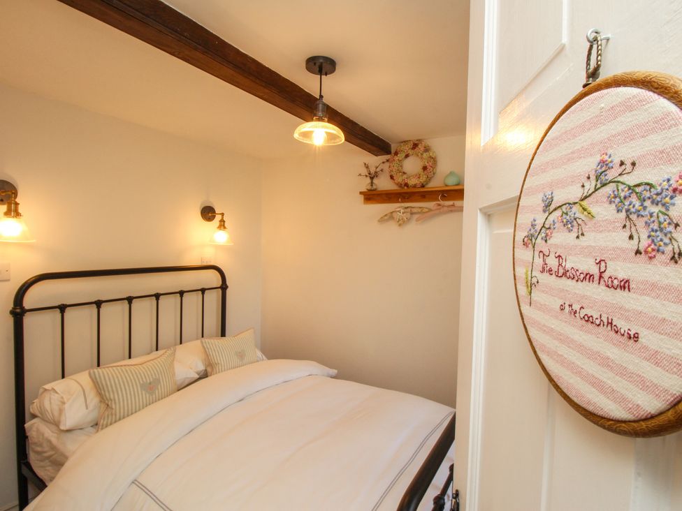 A bedroom with a metal bed frame white bedding wall lights and a wooden shelf with hangers at The Coach House at Lackington Farm Piddletrenthide