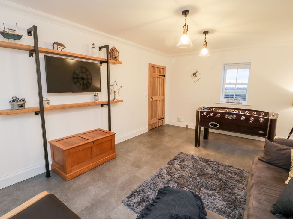 A living room with a wall-mounted television foosball table wooden chest and gray rug at Fell Briggs Cottage Marske-By-The-Sea