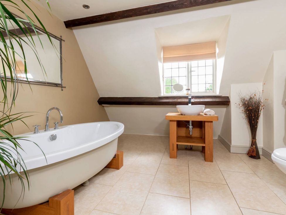 A bathroom with a bathtub wooden sink stand a window and a dried plant at Little Gables in Broadway