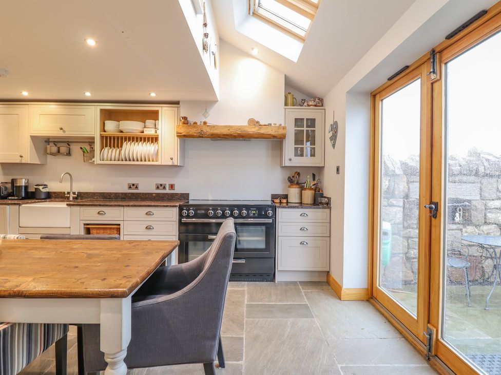 A kitchen with wooden table gray chairs built-in cupboards and double glass doors at Ty Gwyn Cottage in Colwyn Bay