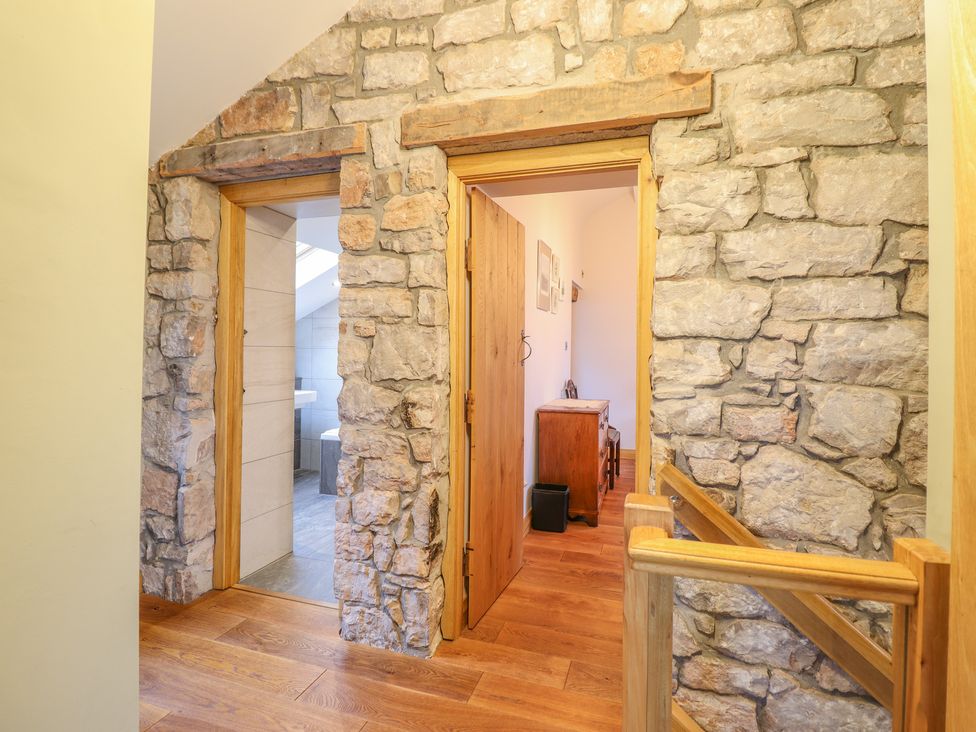 A hallway with wooden floors stone walls and two doorways one leading to a bathroom at Ty Gwyn Cottage in Colwyn Bay