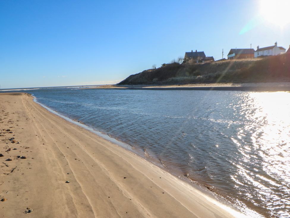 A sandy beach with water and houses on a hill in the background at Wansbeck View 2 in Ashington