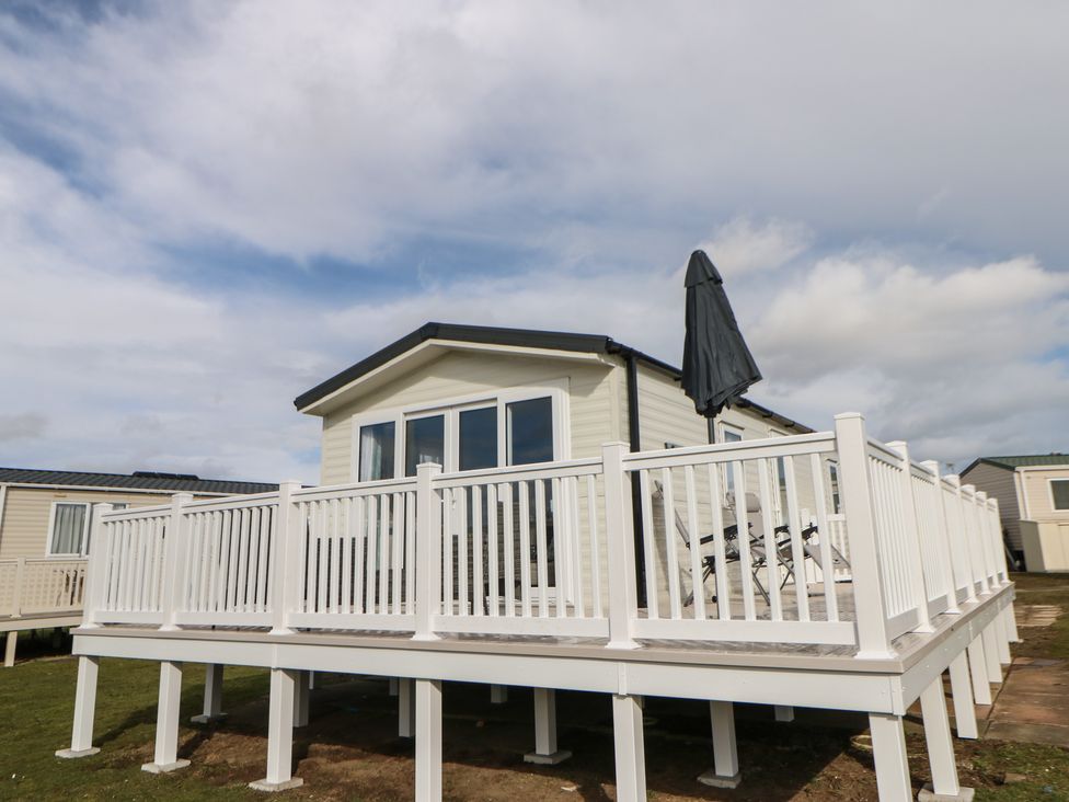 A raised white deck with railing and outdoor chairs next to a small house at Wansbeck View 2 in Ashington