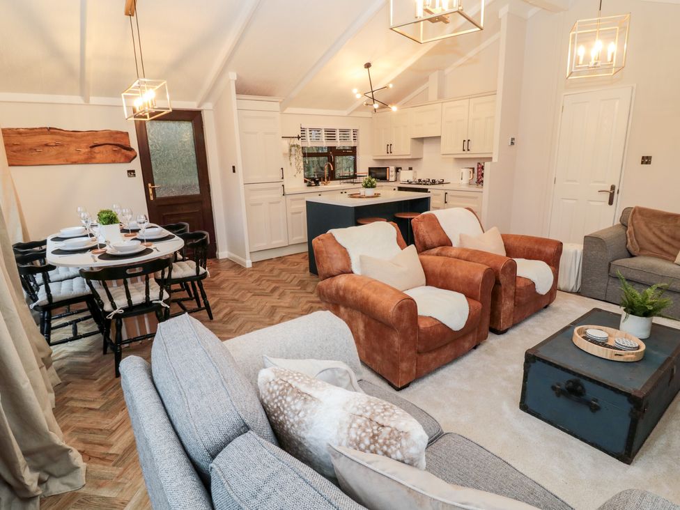 An open plan living room and kitchen with brown armchairs a gray sofa a dining table with chairs and a kitchen island at The Treeline in Swarland near Felton