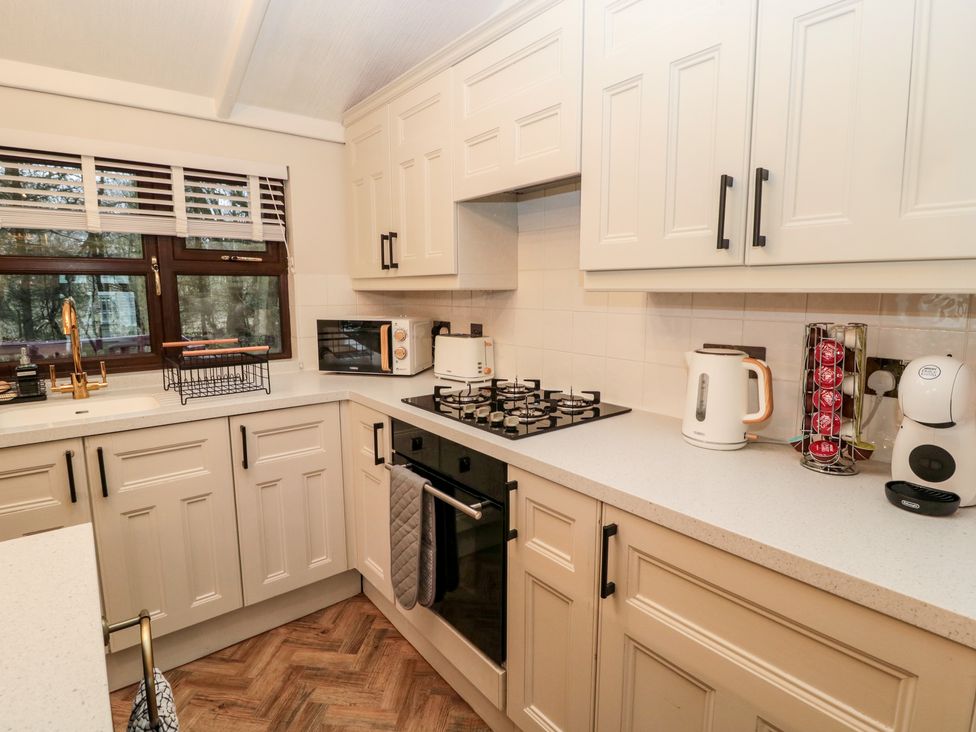 A kitchen with white cabinets a gas stove a microwave toaster kettle and coffee machine at The Treeline in Swarland near Felton