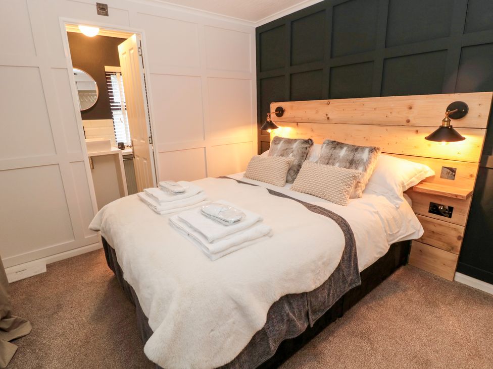 A bedroom with a double bed with wooden headboard and bedside lamps at The Treeline in Swarland near Felton