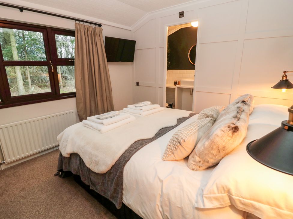 A bedroom with a double bed towels on the bed a window and a door to a bathroom at The Treeline in Swarland near Felton