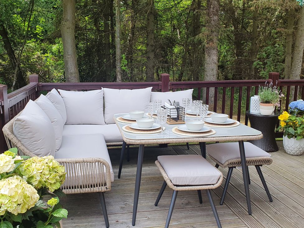 An outdoor dining area with a cushioned corner sofa table and stools surrounded by potted plants at The Treeline in Swarland near Felton