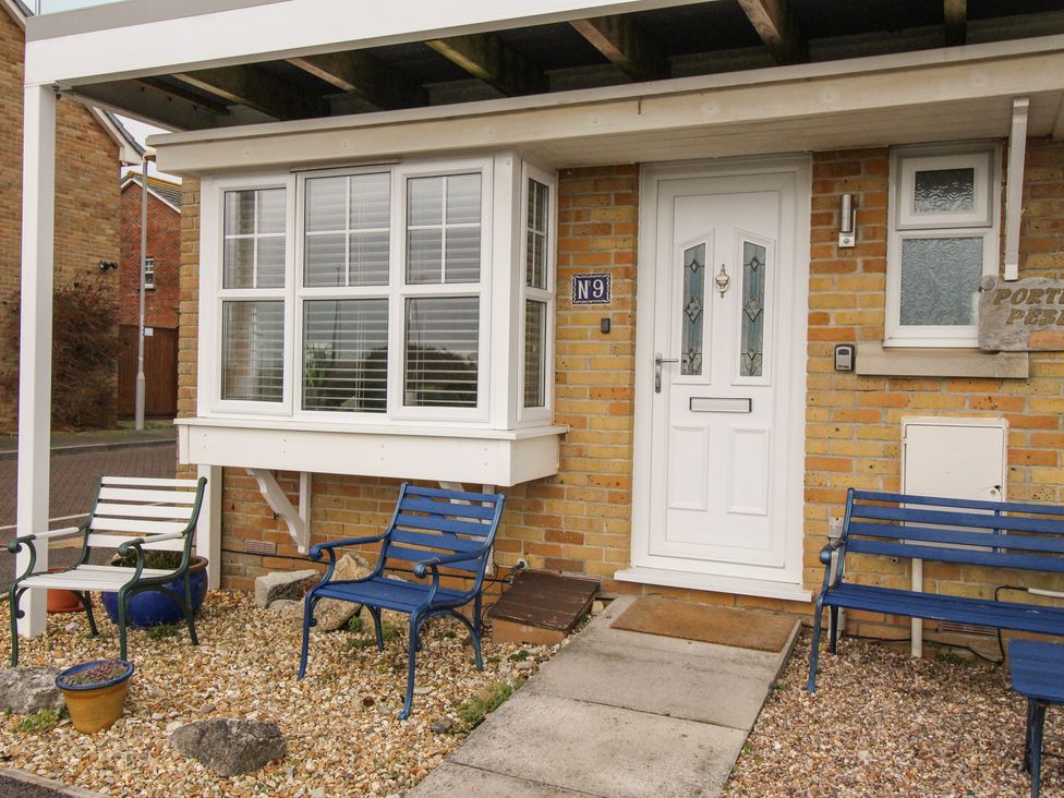 Front entrance of brick house with white door and window and blue and white garden chairs at Portland Pebble in Wyke Regis