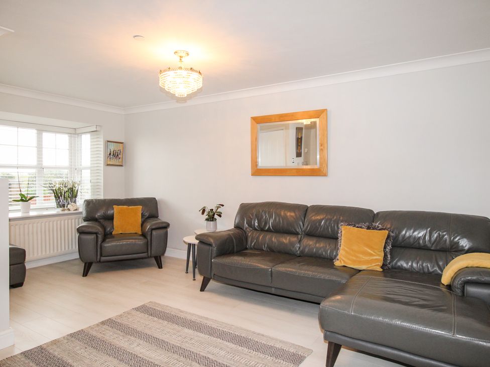 A living room with leather sofas a rug a mirror on the wall and windows at Portland Pebble in Wyke Regis