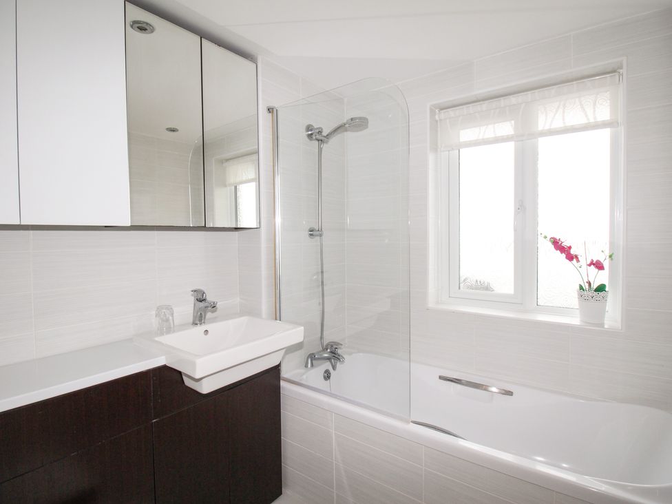 A bathroom with a bathtub shower combination sink with cabinet and a window with a potted plant at Portland Pebble in Wyke Regis