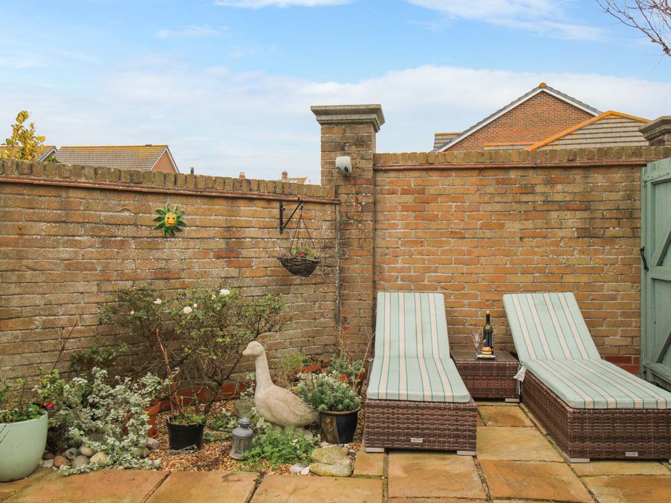 A small outdoor patio with two lounge chairs a side table a bottle of wine and plants at Portland Pebble in Wyke Regis