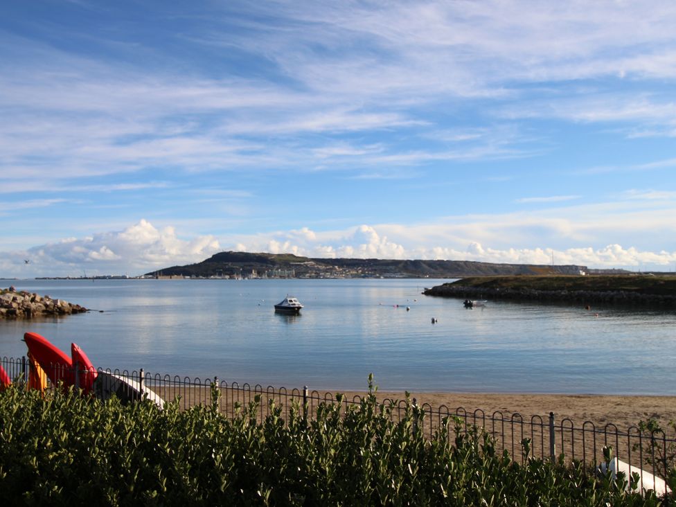 A coastal view with boats on water and a hill in the background at Portland Pebble in Wyke Regis