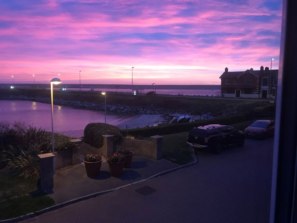 A coastal road with parked cars and street lamps near a rocky shoreline at sunset at Portland Pebble in Wyke Regis