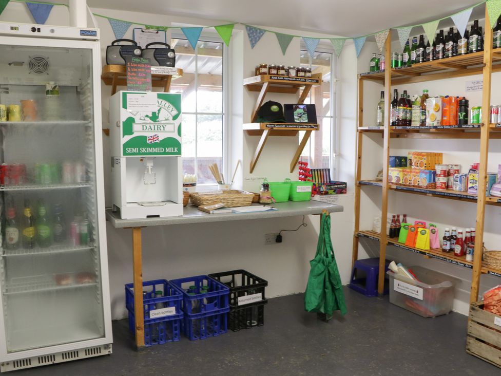 A small shop area with shelves of groceries a milk dispenser crates for bottles and a refrigerated display at Dew Pond in Blagdon