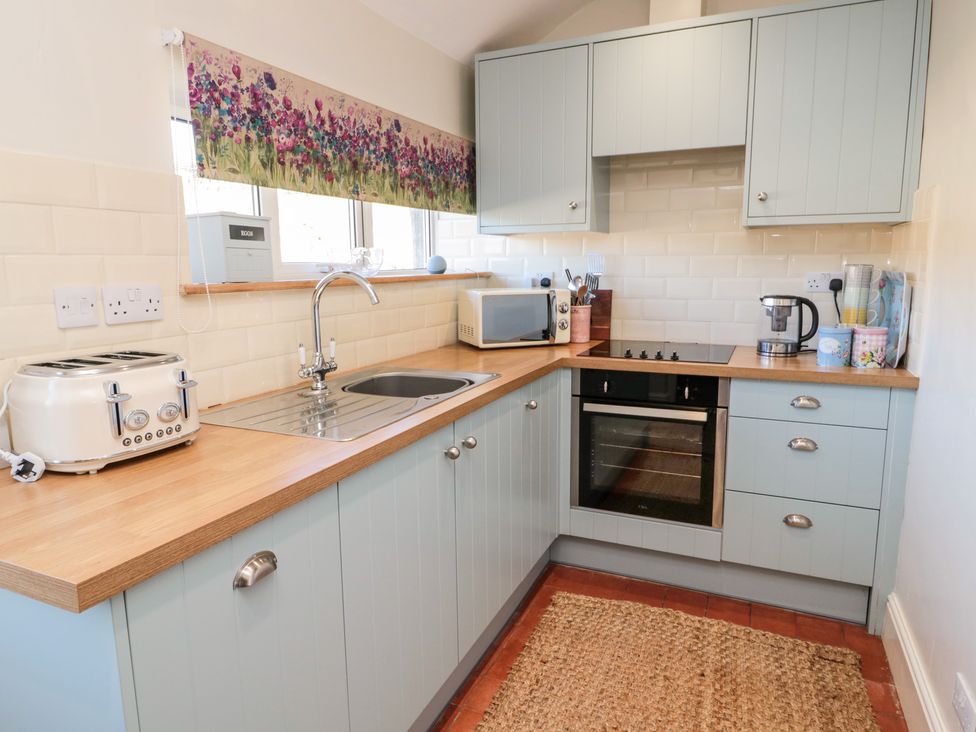 A kitchen with light blue cabinets a toaster a microwave a coffee maker and a sink at Healey Farm Cottage Rothbury