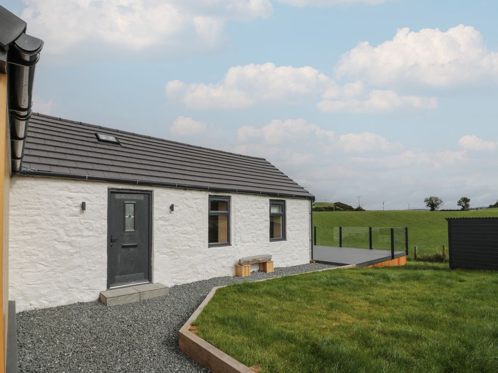 A white stone cottage with a black door and windows next to a gravel path and lawn at Hardhills Cottage in Castle Douglas